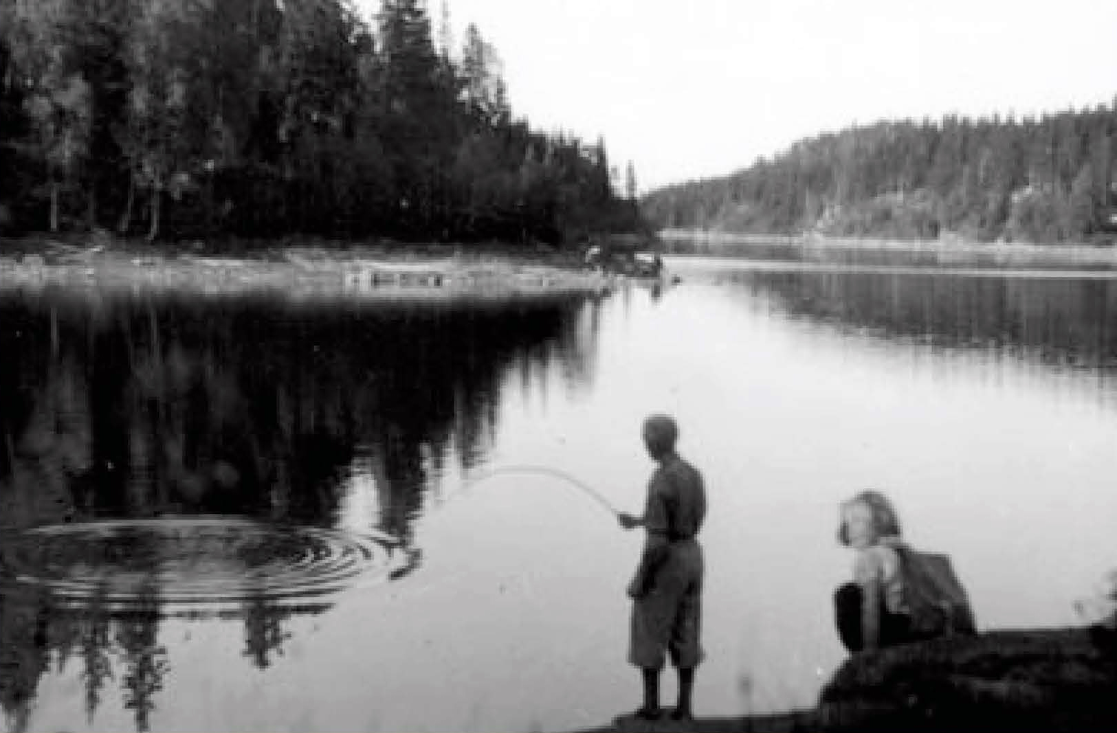 Det er Olaug som sitter på berget nede på Tangen og venter på fiskenapp sammen med en besøkende. Odden som stikker ut rett over «Vika» er eiendomsgrensen mellom Mariholtet og Ellingsrud.