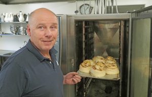 Roy Knutsen har bakt ca. en million kanelboller til gjestene på Vangen – og gitt et solid bidrag til friluftslivet og folkehelsa Her er en ny ladning på vei inn i ovnen. Foto: Bjarne Røsjø.